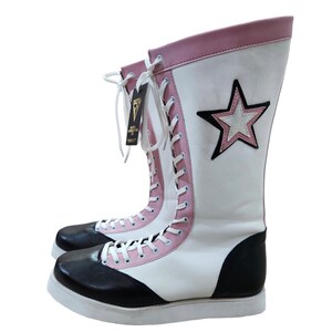 May include: White wrestling boots with black and pink accents. The boots have a star design on the side and a lace-up closure.