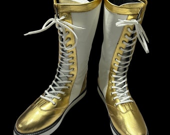 Puede incluir: Un par de botas de boxeo blancas y doradas con cordones blancos. Las botas tienen una parte superior de cuero dorado y una suela blanca.