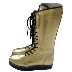 May include: Gold wrestling boots with black laces. The boots are tall and have a thick sole.