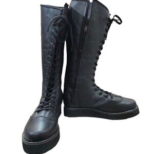 May include: A pair of black leather knee-high boots with lace-up fronts and side zippers. The boots have a thick platform sole.