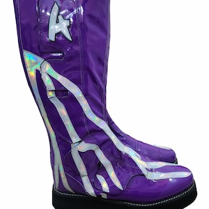 Könnte beinhalten: Ein Paar glänzende, kniehohe Stiefel in Lila. Die Stiefel haben ein silbernes, schillerndes Design und eine schwarze Sohle. Ein silberner Buchstabe "A" befindet sich an der Seite des Stiefels. Die Stiefel haben eine Plateausohle und sind aus glänzendem Material.