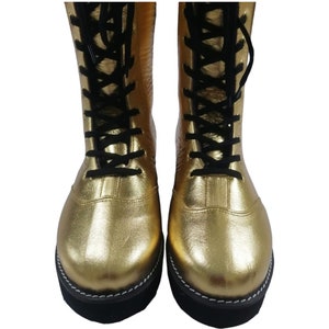 May include: Pair of gold wrestling boots with black laces. The boots have a black sole with white stitching.