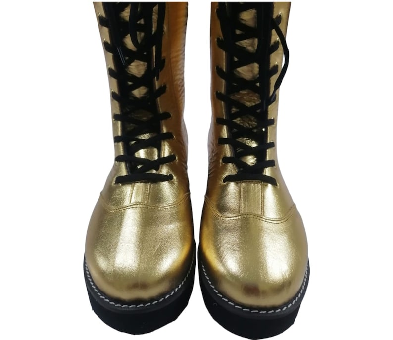 May include: Pair of gold wrestling boots with black laces. The boots have a black sole with white stitching.