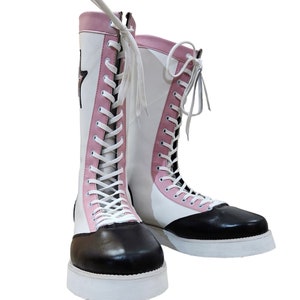 May include: A pair of white and pink high-top boots with black leather toes and white laces. The boots have a white platform sole.