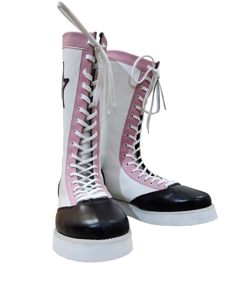 May include: A pair of white and pink high-top boots with black leather toes and white laces. The boots have a white platform sole.