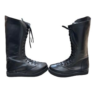 Puede incluir: Un par de botas negras de cuero hasta la rodilla con cordones en la parte delantera y suelas gruesas.