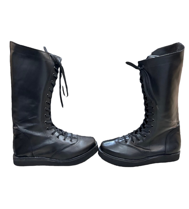 Puede incluir: Un par de botas negras de cuero hasta la rodilla con cordones en la parte delantera y suelas gruesas.