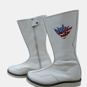 Könnte beinhalten: Ein Paar weiße Lederstiefel mit Reißverschluss und einem dekorativen Grafik eines Schädels mit einem amerikanischen Flaggen-Design. Die Stiefel haben eine schwarze Einfassung und eine weiße Sohle.
