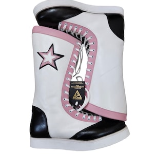 May include: White leather wrestling boots with black accents and pink trim. The boots have a star design on the side and a white lace-up closure. The boots are sitting on a white surface.