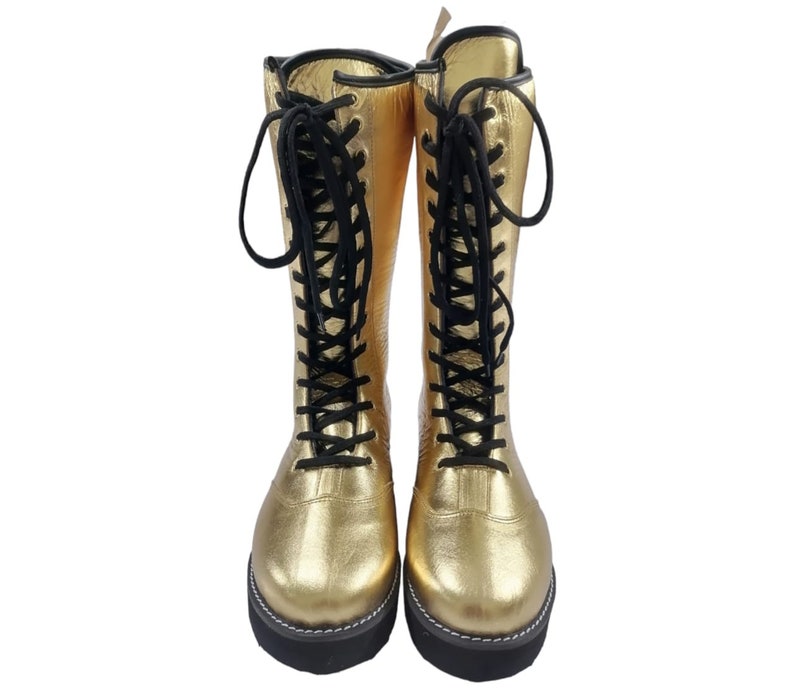 May include: A pair of gold leather wrestling boots with black laces. The boots have a thick sole and are laced up the front.