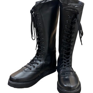 Puede incluir: Un par de botas negras de cuero hasta la rodilla con cordones en la parte delantera y suelas gruesas.
