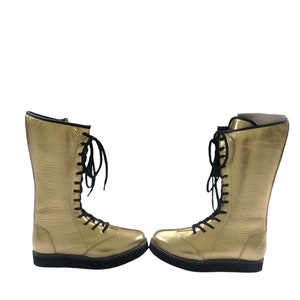 May include: A pair of gold wrestling boots with black laces. The boots are made of leather and have a thick rubber sole.