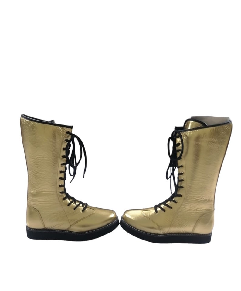 May include: A pair of gold wrestling boots with black laces. The boots are made of leather and have a thick rubber sole.