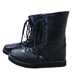 Puede incluir: Botas de cuero negro con cordones, suela gruesa y costuras blancas.