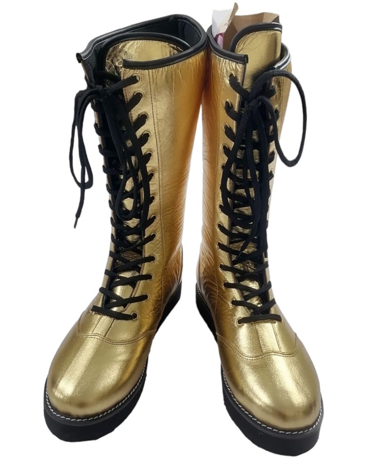 May include: A pair of gold leather wrestling boots with black laces. The boots have a thick black sole and are laced up the front.