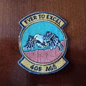 May include: A blue and gold embroidered patch with a bald eagle in flight. The patch reads "Ever to Excel" and "405 AGS".