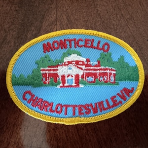 May include: Oval patch featuring Monticello, with the text "MONTICELLO CHARLOTTESVILLE VA." in red lettering. The building is depicted in red and white, set against a blue background with a yellow border. The patch is likely a souvenir.