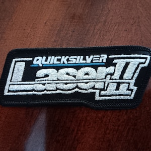 May include: Black embroidered patch with white stitching. The patch features the text "QUICKSILVER" in blue and "Laser II" in white.