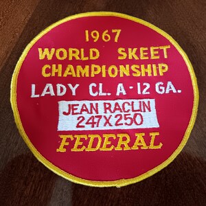 May include: A red and yellow circular patch with the text "1967 WORLD SKEET CHAMPIONSHIP LADY CL. A-12 GA. JEAN RACLIN 247X250 FEDERAL"