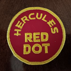 May include: A red circular patch with yellow embroidered text that reads "Hercules Red Dot".