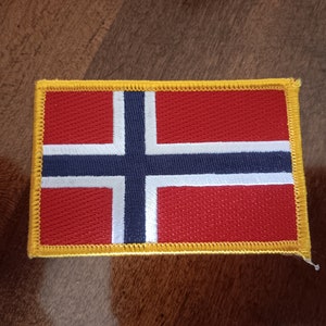May include: A red, white, and blue embroidered patch with a yellow border, depicting the flag of Norway.