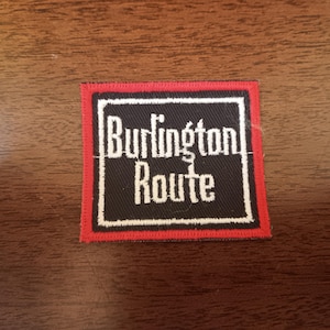 May include: A red and black embroidered patch with the text "Burlington Route" in white.