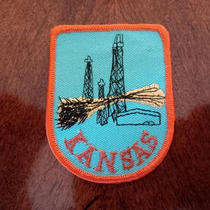 May include: An orange and blue embroidered patch with an image of oil derricks and the text "C.N.S.A.S."