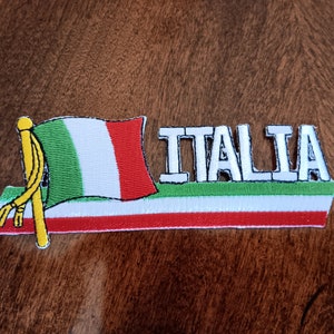 May include: Embroidered patch featuring the Italian flag and the word "ITALIA". The flag has green, white, and red stripes. The word "ITALIA" is in white letters with a black outline.