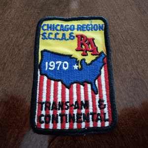 May include: Embroidered patch with the text "CHICAGO REGION S.C.C.A. RA 1970 TRANS-AM & CONTINENTAL" on a yellow, blue, and red background. The patch features a map of the United States and is bordered in black.