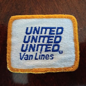 May include: A white patch with a yellow border, featuring the text "UNITED UNITED UNITED" in blue lettering, followed by "Van Lines" in blue lettering with a registered trademark symbol.