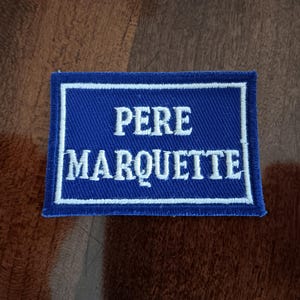 May include: A blue embroidered patch with white stitching that reads "Pere Marquette".