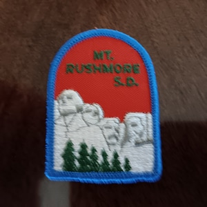 May include: A blue and white embroidered patch with the text "MT. RUSHMORE S.D." and an image of Mount Rushmore National Memorial.