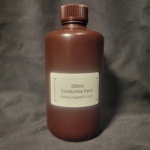 Puede incluir: Una botella de plástico marrón con tapa a juego. La etiqueta dice "250ml Conductive Paint" e "Invictus-SupplyCo.com". La botella contiene un líquido oscuro, probablemente pintura, para proyectos electrónicos.