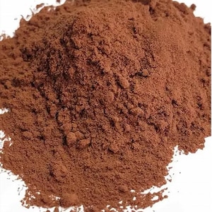 Puede incluir: Primer plano de un montón de polvo fino de color marrón rojizo. El polvo tiene una textura granular y parece estar densamente compactado. El color es uniforme, sin variaciones ni patrones visibles. El fondo es blanco liso.