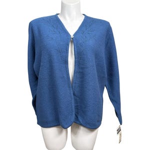 May include: A blue cardigan sweater with a V-neck and long sleeves. The sweater has a single button closure and decorative leaf-like embroidery near the neckline. The bottom hem has a scalloped edge. A tag is attached to the bottom of the sweater.