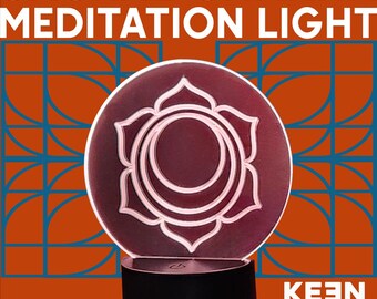 Puede incluir: Una lámpara de meditación del chakra sacro con un diseño circular de color burdeos que presenta un símbolo de flor de loto blanco estilizado. La luz se asienta sobre una base negra, con el texto "SACRAL CHAKRA MEDITATION LIGHT" en la parte superior y "KEEN INDUSTRIES" en la inferior.
