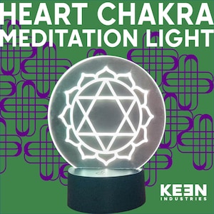 May include: A round, illuminated Heart Chakra Meditation Light with a white geometric design. The light sits on a black base, with the text "HEART CHAKRA MEDITATION LIGHT" above it. The background is green with a purple pattern, and the Keen Industries logo is visible.