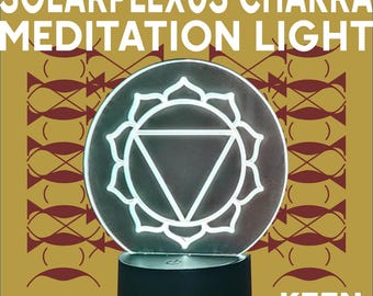 Puede incluir: Una luz de meditación del chakra del plexo solar redonda e iluminada. La luz presenta un diseño geométrico blanco dentro de un círculo, sobre una base negra. Las palabras "SOLAR PLEXUS CHAKRA MEDITATION LIGHT" se muestran en letras blancas.
