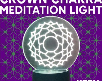 Puede incluir: Una luz redonda e iluminada con un diseño floral blanco, con la inscripción "CROWN CHAKRA MEDITATION LIGHT". La luz se encuentra sobre una base negra, sobre un fondo púrpura con un patrón de estrellas verdes. El logotipo de Keen Industries es visible.