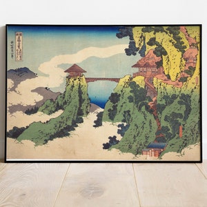 May include: A vintage Japanese woodblock print depicting a mountain landscape with a bridge, houses, and clouds. The print is framed in black and has Japanese text in the upper left corner.