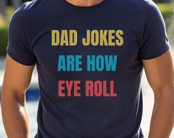 Op de afbeelding: Een marineblauw t-shirt met de tekst "DAD JOKES ARE HOW EYE ROLL" in kleurrijke letters.