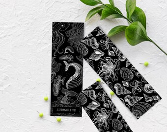 May include: Black and white illustrated bookmarks with a nautical theme. The bookmarks feature detailed drawings of sea creatures like whales, octopuses, and seashells. One bookmark has the word "SUBMARINE" at the bottom. The bookmarks are arranged on a white surface.