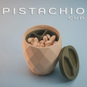 Könnte beinhalten: Eine beige, geometrisch gemusterte Tasse gefüllt mit Pistazien, mit einem passenden Deckel daneben. Der Text "PISTACHIO CUP" wird über der Tasse angezeigt. Die Tasse hat ein dunkelgrünes Innere.