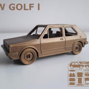 Könnte beinhalten: Ein bronzefarbenes Modellauto eines VW Golf I. Das Miniaturfahrzeug verfügt über detaillierte Räder, Fenster und Karosserieteile. Der Text "VW GOLF I" steht über dem Auto. Rechts befindet sich eine Zeichnung der Autoteile.