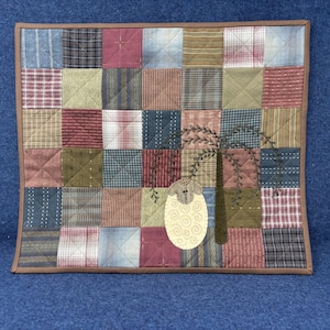 May include: A patchwork quilt with a brown border. The quilt features squares of various fabrics in shades of red, blue, green, and tan. A tree and sheep applique are on the quilt.