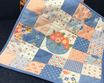 May include: A blue and peach patchwork quilt with a floral applique in the center. The quilt is made of various fabrics with floral and geometric patterns.