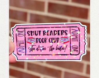 May include: A pink ticket-shaped sticker with the text "SMUT READERS BOOK CLUB" and "The dirtier the better!" in black and purple. The sticker has a holographic, glittery effect and features a stack of books.