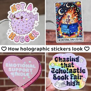 May include: Four holographic stickers with different designs. The first sticker is a purple and pink pufferfish with the text "Not a Hugger". The second sticker is a skeleton in a dumpster with flames and the text "The Emotional Dumpster Fire". The third sticker is a pink heart with the text "Emotional Support Kindle". The fourth sticker is a rainbow with the text "Chasing that Scholastic Book Fair High".