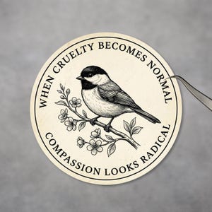 May include: A round sticker with a black and white illustration of a bird perched on a flowering branch. The text around the edge reads "WHEN CRUELTY BECOMES NORMAL COMPASSION LOOKS RADICAL."