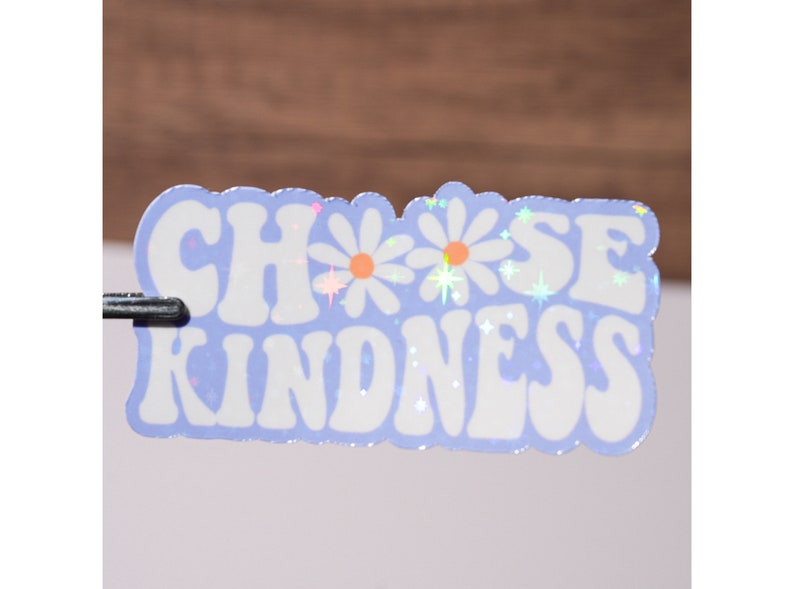 May include: A light blue sticker with the text "CHOOSE KINDNESS" in white, with two white daisies and glitter accents.
